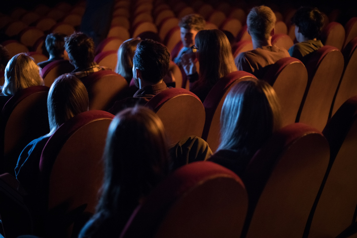 Back view of a group of young adult people sitting in the cinema and watching funny movie. They laughing and having fun.
